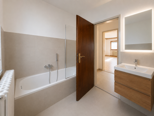 Modernes Badezimmer mit Badewanne, Holzvasen und beleuchtetem Spiegel, helle Wände.